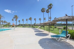 A poolside area with lounge chairs, palm trees, and a water slide. - Las Americas in Islantilla (Isla Cristina)