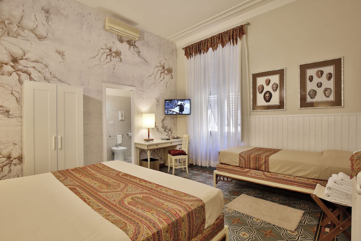 A hotel room with two beds, a desk, a TV, and artwork on the walls.