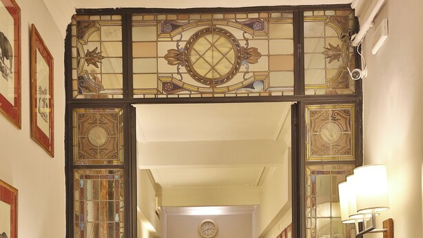A hallway with checkered flooring, a wooden table with a lamp, a chair, and a trunk with decorative items. - MADAMA GUEST HOUSE (Florence)