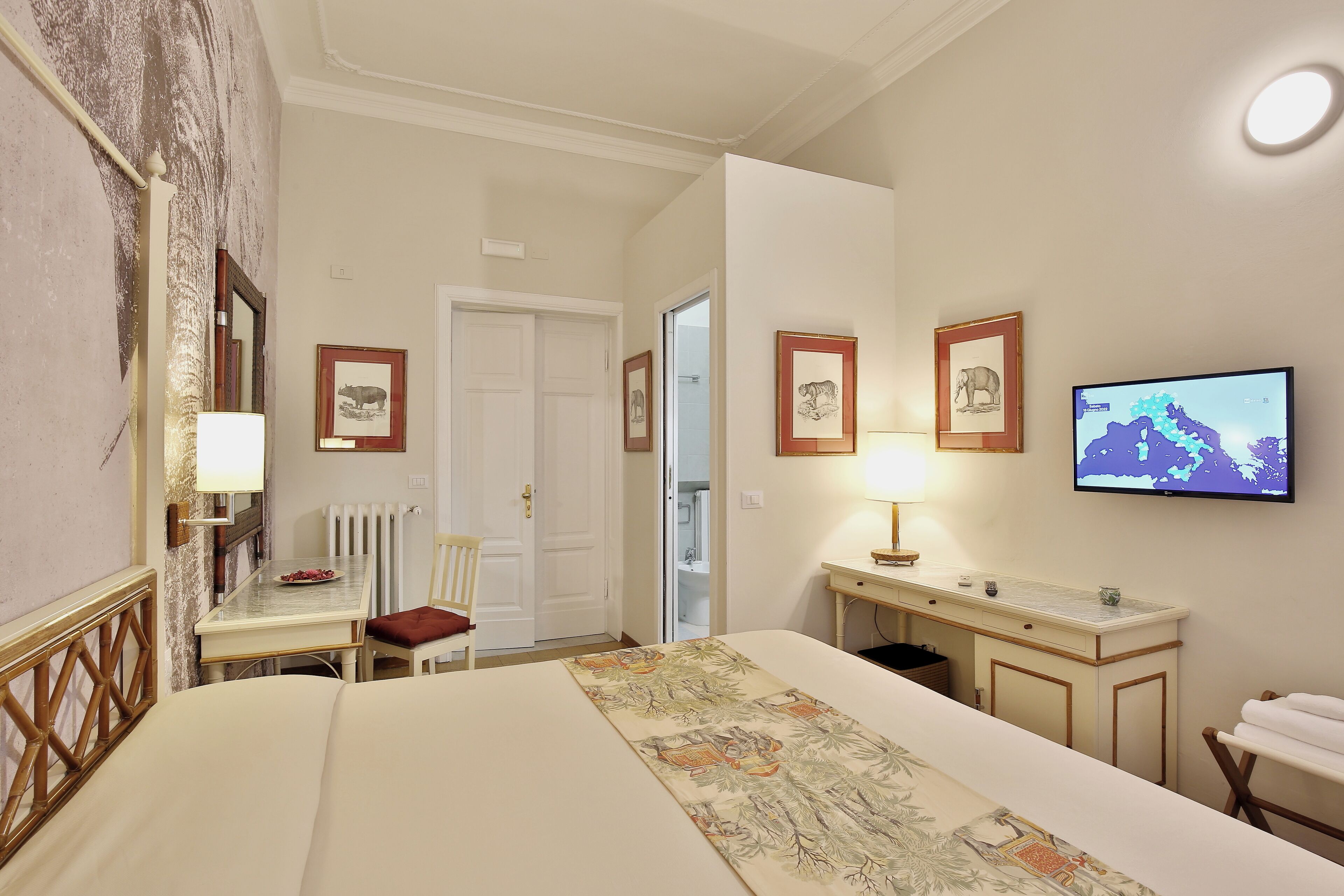 A hotel room with a bed, a desk, a chair, a television, and framed pictures on the wall.