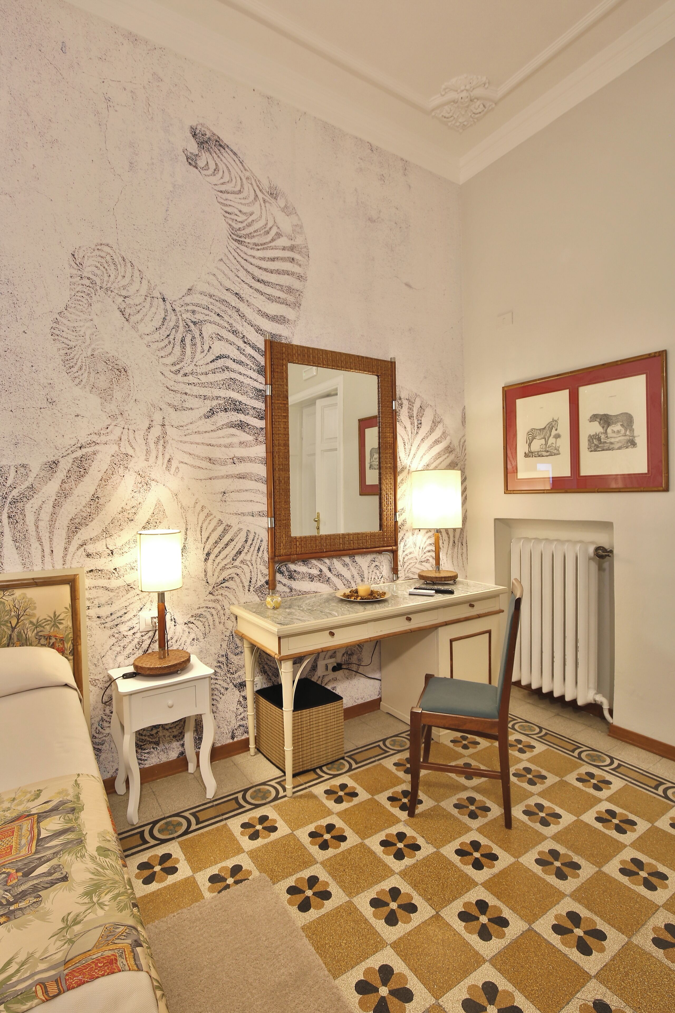 A bedroom with a bed, a desk, a chair, a lamp, a radiator, and a patterned carpet.