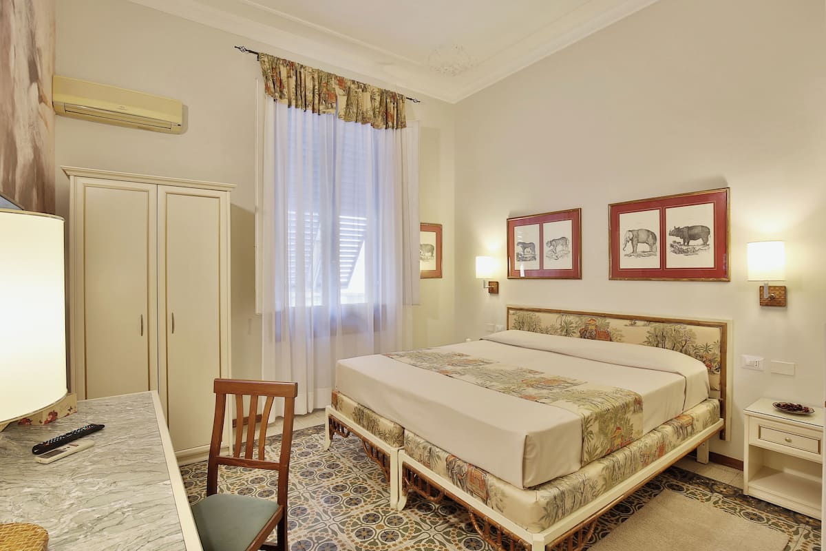 A hotel room with a bed, a desk, a chair, a wardrobe, and a nightstand.