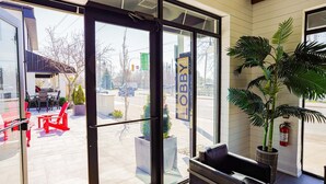 A modern lobby with large glass doors, a seating area with red chairs, and a large potted plant. - Colonial Hotel & Suites - Brenner Premium King (Grand Bend)