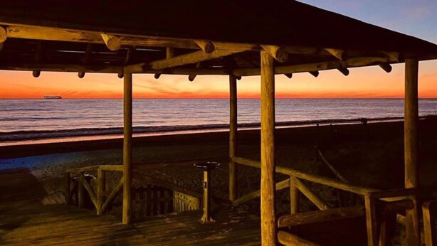 Eine hölzerne Steg mit einem überdachten Bereich, der auf den Sonnenuntergang über dem Meer blickt.