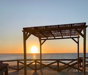 Une jetée en bois surmontée d’une structure au toit de chaume, d’où l’on a une vue sur l’océan au coucher du soleil.