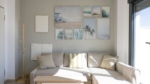 Ein Wohnzimmer mit einem beigen Sofa, einem Holztisch und einer Wand, die mit Küstenkunstwerken verziert ist.
