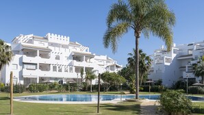 Ein weißes Gebäude mit Balkonen, einem Swimmingpool und Palmen.
