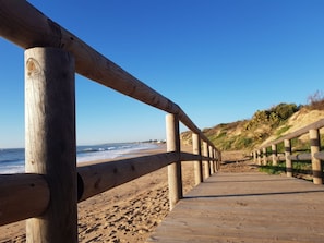 Une promenade en bois menant à une plage, avec un ciel dégagé.