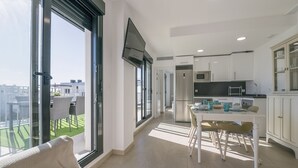 Eine moderne Küche mit weißen Schränken, eine Essecke mit Tisch und Stühlen sowie große Fenster mit Blick auf die Stadt.
