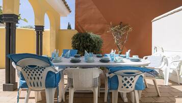 An outdoor dining area with a table set for four, surrounded by white chairs with blue accents.