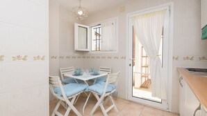 A small kitchen with a dining area. There is a table with chairs, a window with curtains, and a sink. - Los Jandalos in El Puerto de Santa Maria (El Puerto de Santa Maria)