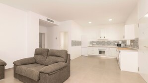 A modern living room with a grey sofa, a kitchen with white cabinets and patterned backsplash, and a small dining area. - Miamar 1 in Hozanejos (Chiclana de la Frontera)