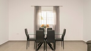 A dining area with a glass table and black chairs, a vase with flowers, and a window with curtains. - Miamar 1 in Hozanejos (Chiclana de la Frontera)