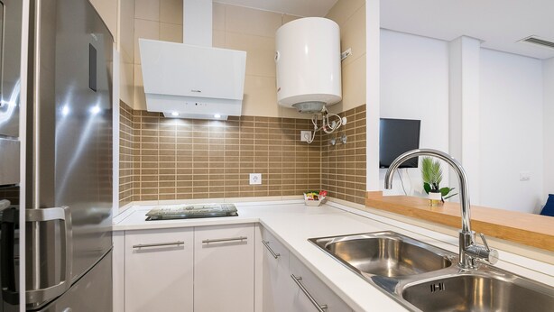 Una cocina moderna con electrodomésticos de acero inoxidable, un lavamanos doble y un salpicadero de azulejos blancos.