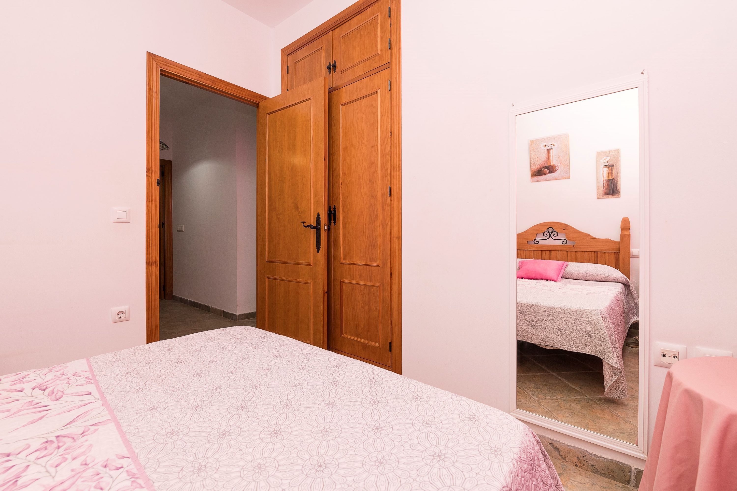 Ein Schlafzimmer mit einem Bett, einem Holzschrank und einem Spiegel, der ein Bett und Wandbilder reflektiert.