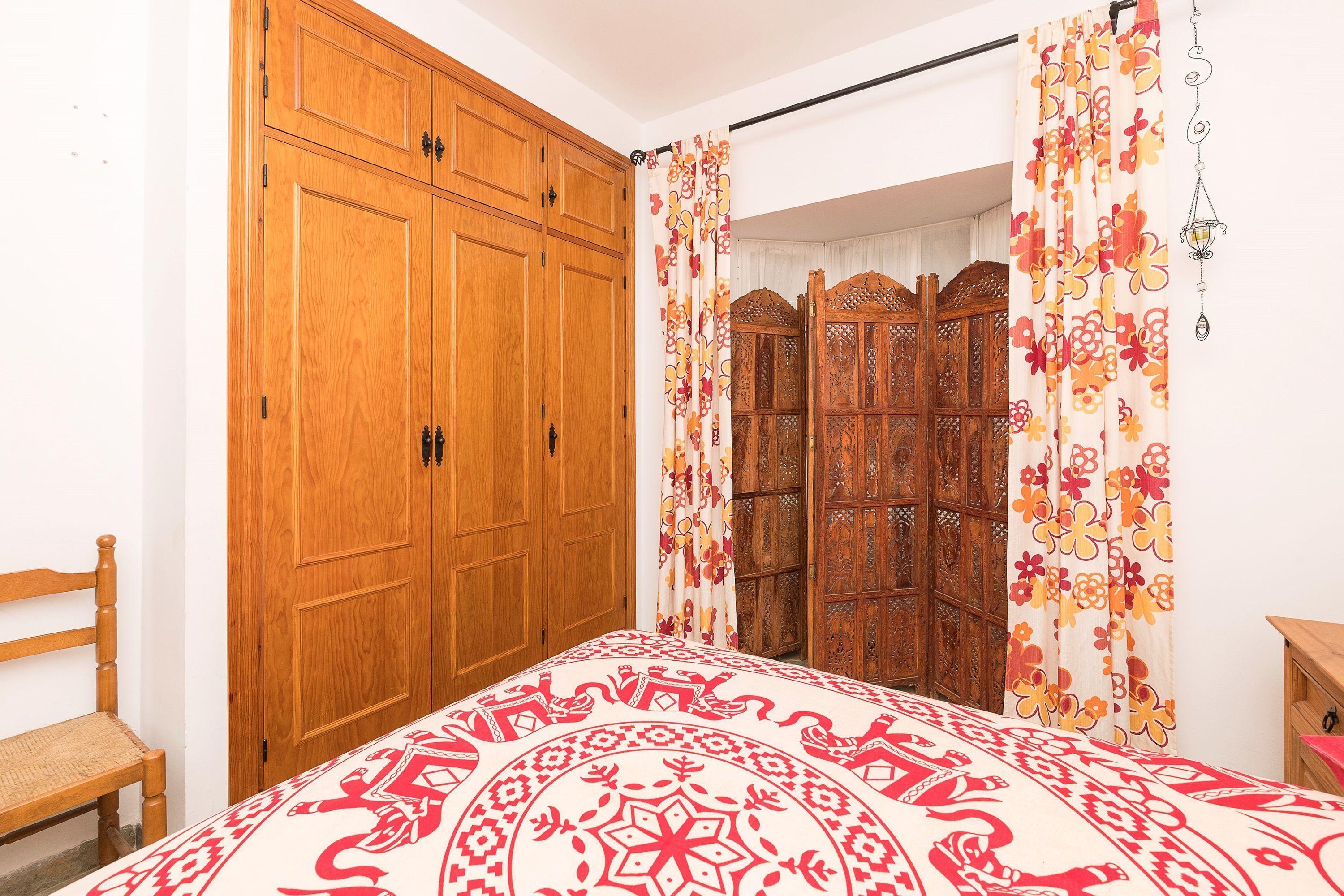 Une chambre à coucher avec une armoire en bois, un lit recouvert d’une couvre-lit à motifs et un rideau décoratif.