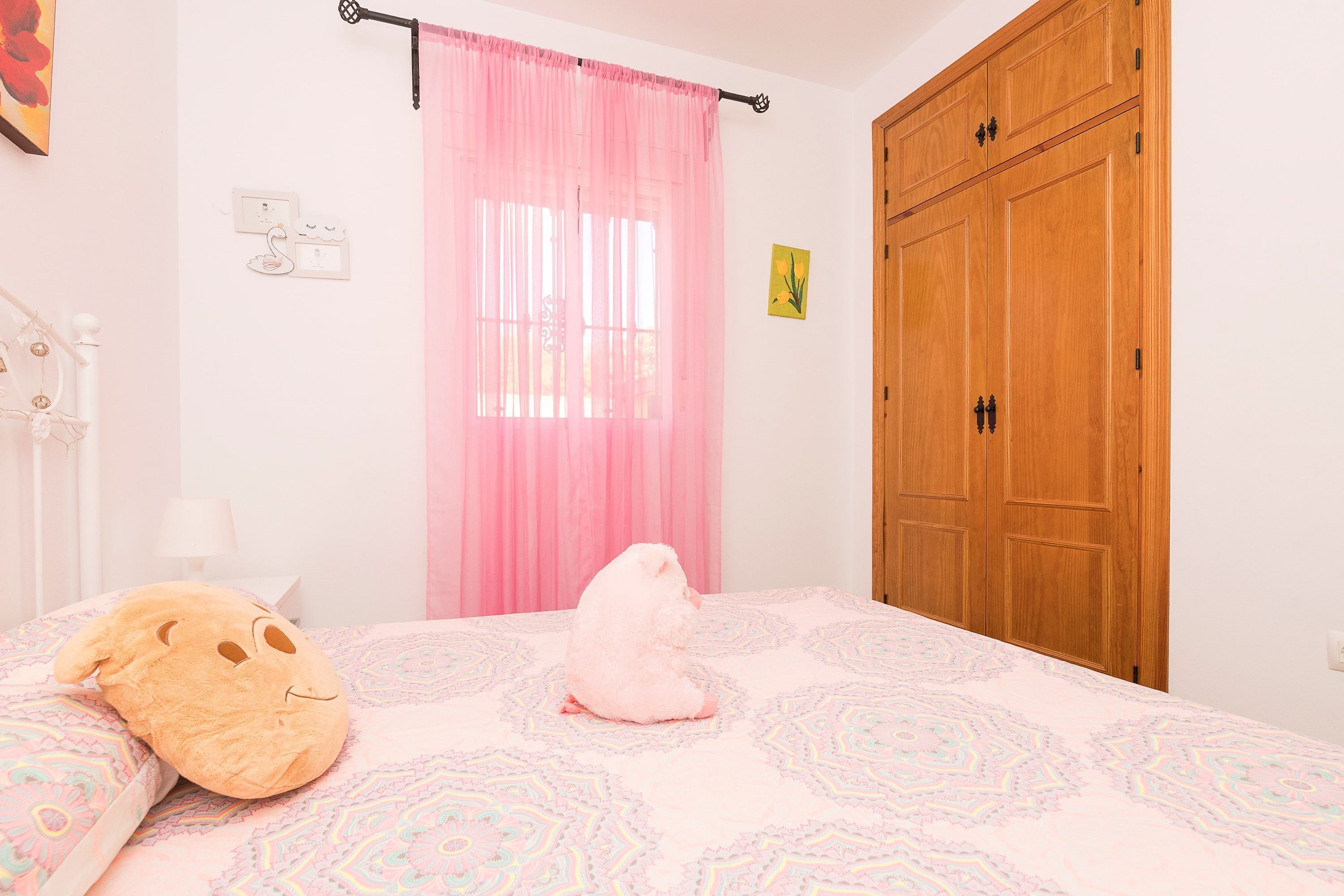 A bedroom with a bed, a pink curtain, a wooden wardrobe, and a wall socket.