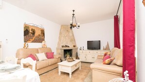 A living room with beige sofas, a white coffee table, a stone fireplace, and a flat-screen TV.