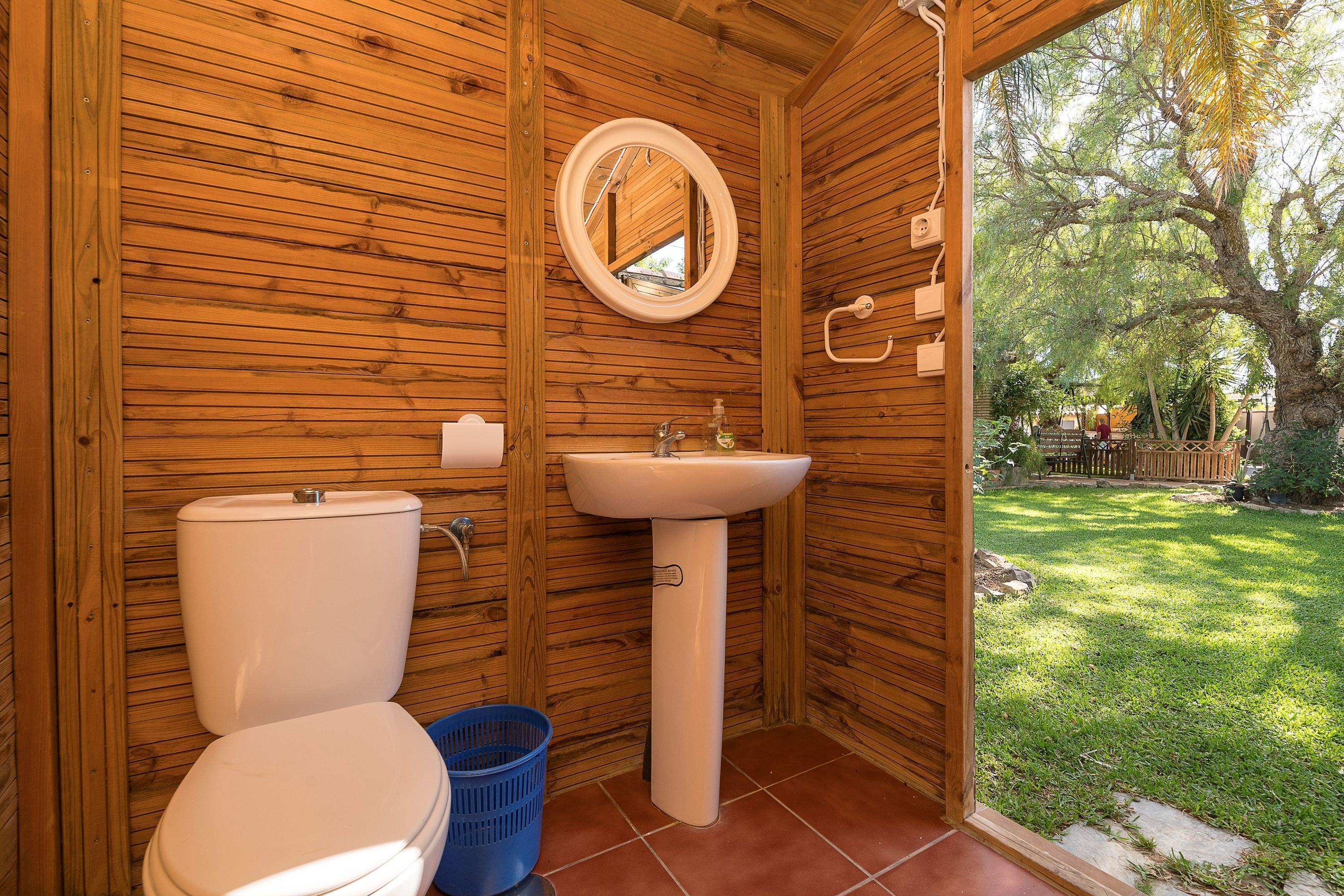 A wooden bathroom with a toilet, sink, and mirror.