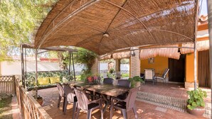 An outdoor patio with a wooden table and chairs, a covered seating area, and potted plants.