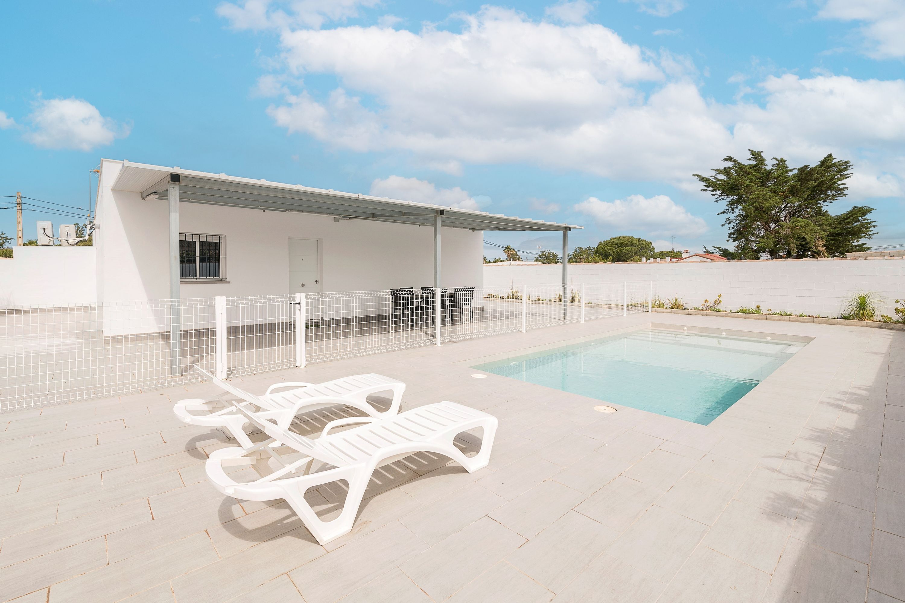 A pool area with white lounge chairs and a covered seating area.