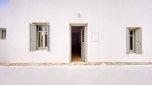 A white building with three open windows and a door, a tiled floor, and a small light fixture above the door.