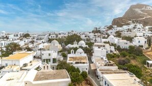 A coastal town with white buildings, a prominent hill, and a clear sky.