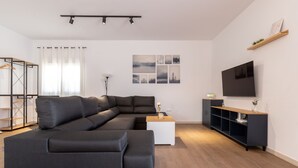 Un salon moderne avec un canapé d’angle, un téléviseur à écran plat et un plancher en bois.