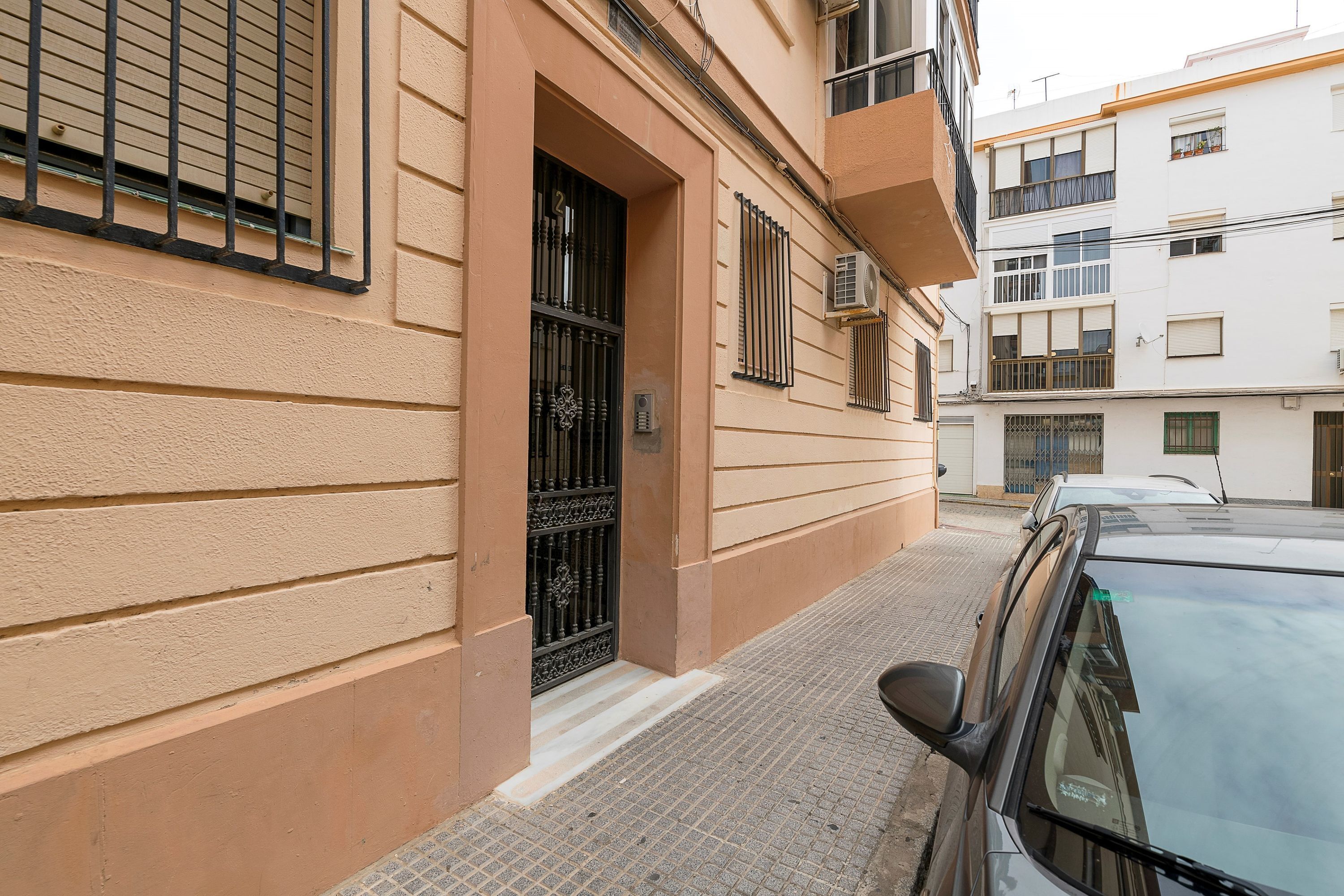 A building with a beige facade, a black metal gate, and a parked car.