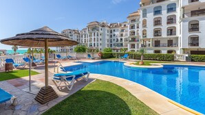 A swimming pool with lounge chairs and umbrellas, surrounded by multi-story buildings with balconies. - Marina De La Duquesa 805 (Manilva)