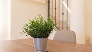 Une plante en pot est posée sur une table en bois dans une pièce où l’on aperçoit un escalier au fond.