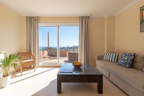 A living room with a sofa, a glass coffee table, a wicker chair, and a potted plant. - Los Lagos in Elviria (Marbella)