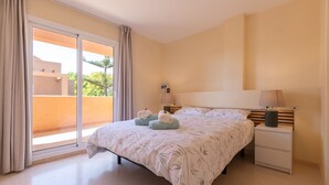 Une chambre à coucher avec un lit, des tables de chevet et une vue sur un balcon extérieur accessible par une porte coulissante.
