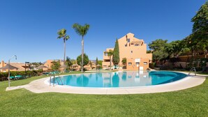Une piscine entourée d’une pelouse bien entretenue, avec un bâtiment doté d’un toit plat et de nombreuses fenêtres en arrière-plan.