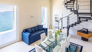 A modern living room with a glass dining table, white chairs, a blue sofa, and a spiral staircase. - Blu Breeze on Seafront (Naples)