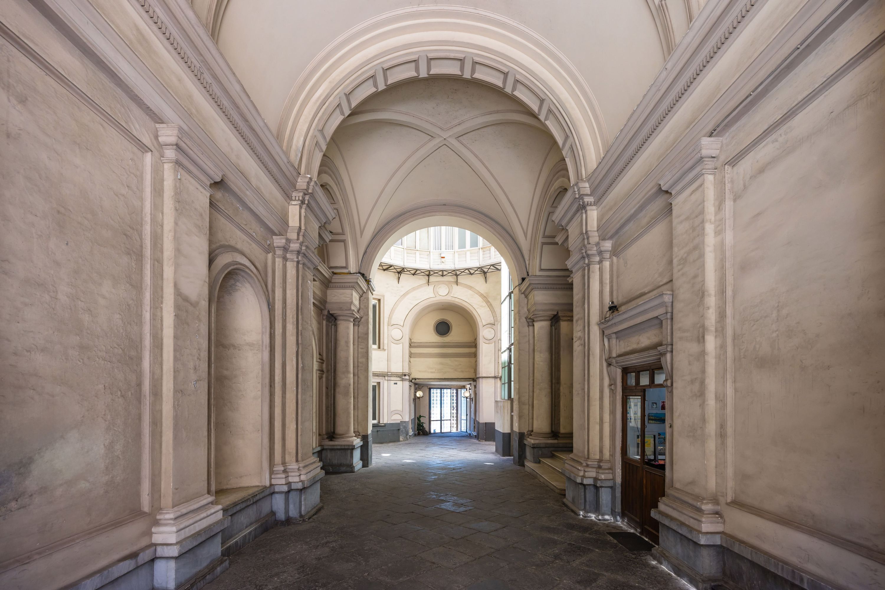 A grand hallway with high ceilings, arched doorways, and classical columns.