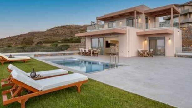 Una moderna casa a due piani con piscina, area salotto esterna e vista sulle colline.