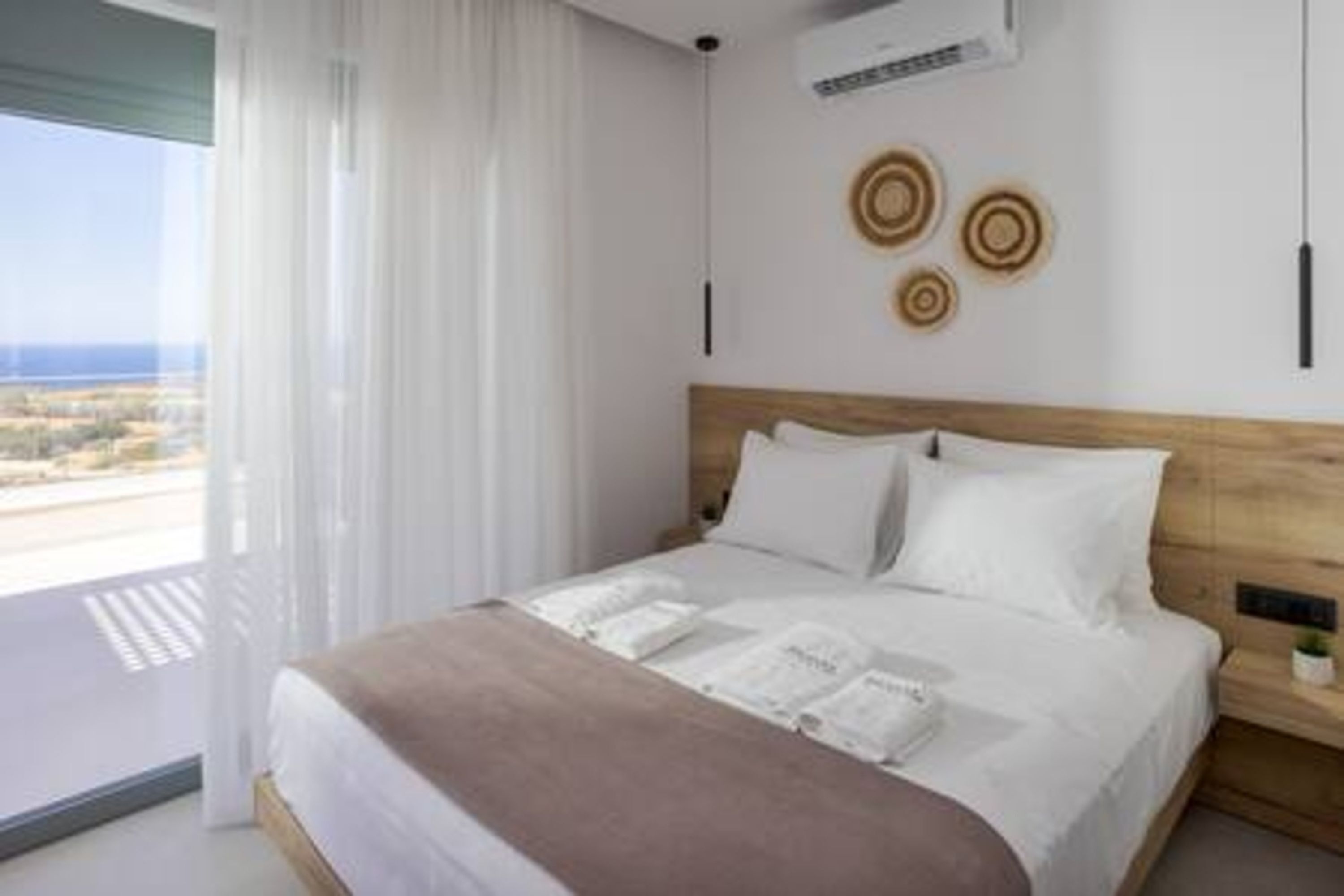 A hotel room with a large bed, a wooden headboard, a nightstand, and a view of the beach.