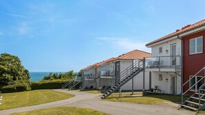 A row of two-story buildings with red-tiled roofs, a pathway leading to the entrance, and a view of the sea in the background. - Gudhjem Søpark Lejl. 43 (Gudhjem)