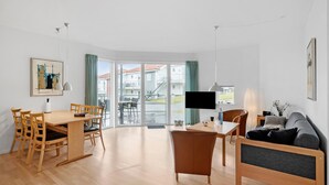 A modern living room with a wooden dining table, a sofa, and a TV. - Gudhjem Søpark Lejl. 43 (Gudhjem)