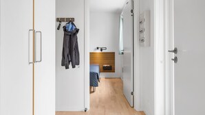 A hallway with a bed, a wooden headboard, a coat rack, and a door leading to a bathroom. - Gudhjem Søpark Lejl. 43 (Gudhjem)