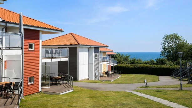 A modern building with a red facade, a balcony with outdoor furniture, and a view of the sea. - Gudhjem Søpark Lejl. 43 (Gudhjem)
