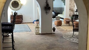 Ein Innenraum mit Steinfußboden, einem Essbereich mit Tisch und Stühlen sowie einem Wohnzimmer mit Sofa und Hocker.