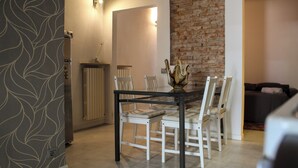 A dining area with a glass table and white chairs, a brick wall, and a radiator. - [Historic House] in the Heart of Bergamo (Bergamo)