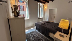 A bedroom with a bed, bedside table, lamp, and a view of a building outside. - [Historic House] in the Heart of Bergamo (Bergamo)