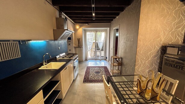 A modern kitchen with a black countertop, stainless steel appliances, and a wooden dining table with chairs. - [Historic House] in the Heart of Bergamo (Bergamo)