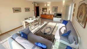 A living room with a sofa, a TV, and a dining area with chairs and a table. - [Exclusive 120 SQM] in the heart of Bergamo (Bergamo)