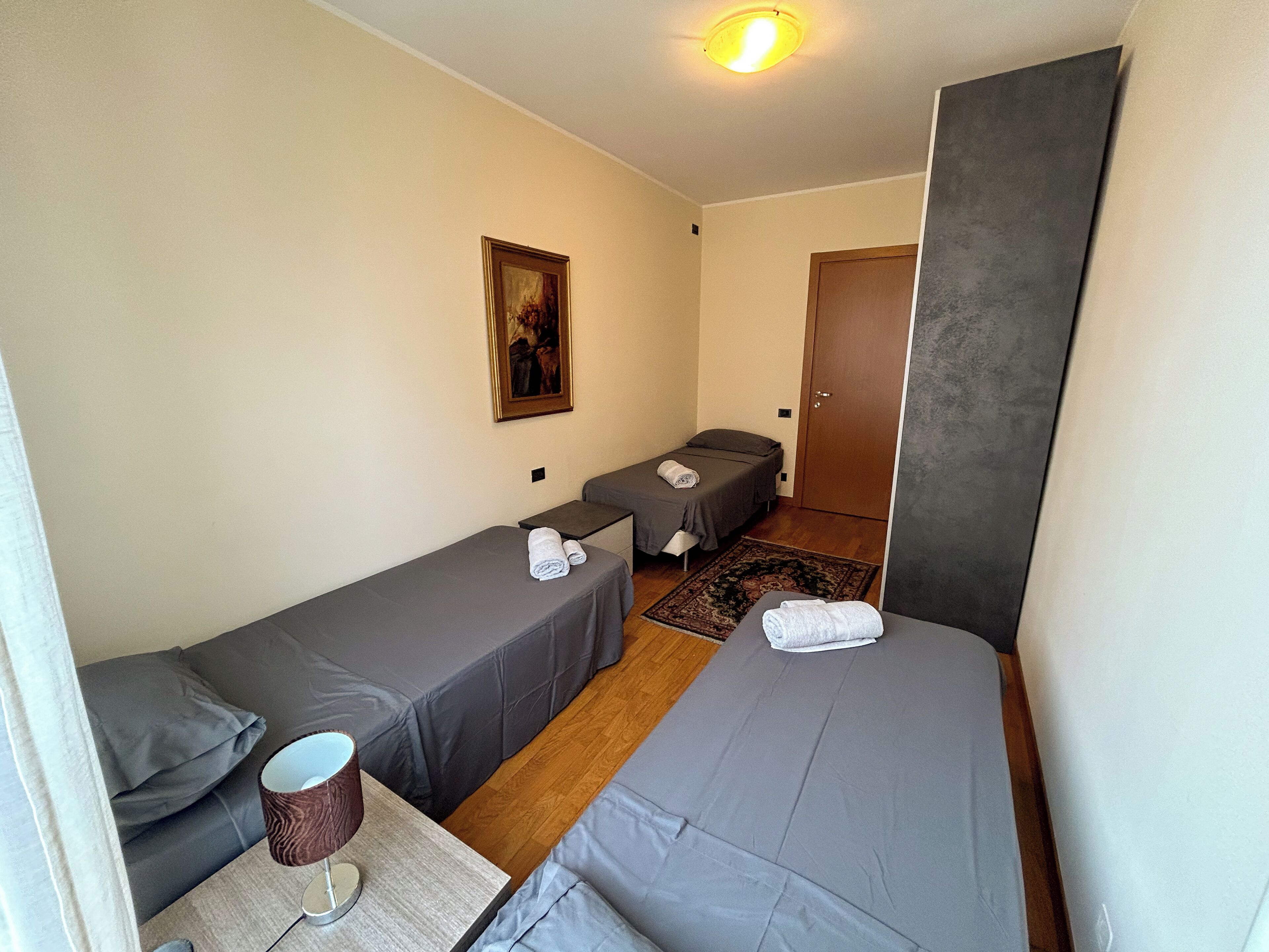 A small, compact room with two single beds, a small table with a lamp, and a door.