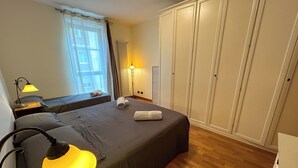 A bedroom with a bed, bedside lamps, a window with curtains, a radiator, and a wardrobe. - [Exclusive 120 SQM] in the heart of Bergamo (Bergamo)