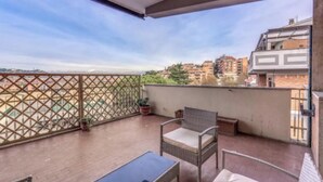 A balcony with wicker furniture, a glass table, and a view of buildings and greenery. - Spacious Apartment Near Saint Peter's Basilica
 (Roma)